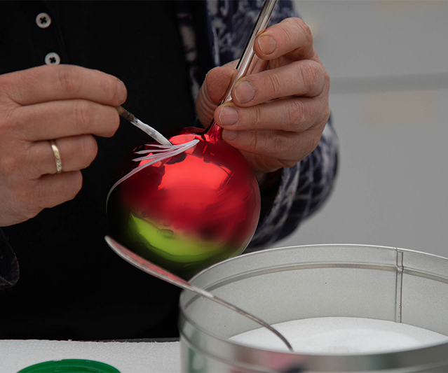 Handpainting Christmas bauble | Glavena Painter is putting glue on a christmas bauble to apply glitter