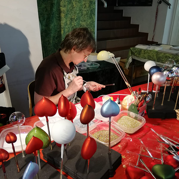 Decorating christmas ornaments | Glavena Glavena owner at a desk with multiple ornaments on it, painting